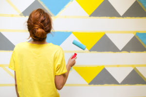 Girl paints the wall in geometric pattern.